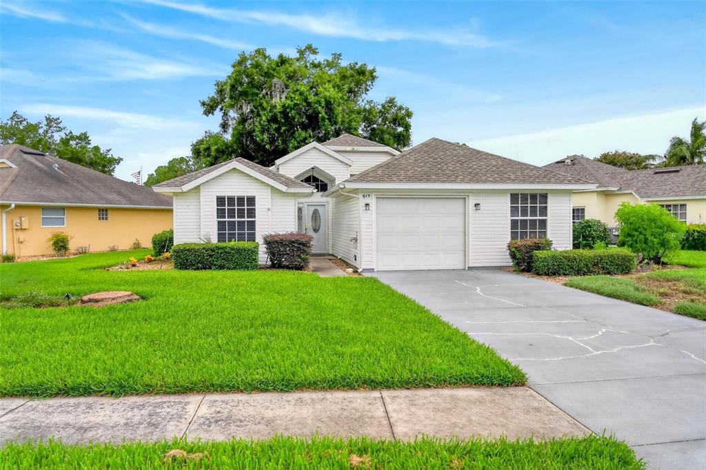 A white single-story house with a garage and a green lawn under a blue sky — 615 JUNIPER WAY, TAVARES, FL