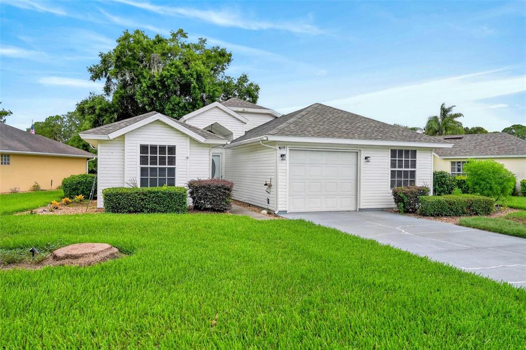 A single-story white house with a garage and a green lawn under a blue sky — 615 JUNIPER WAY, TAVARES, FL