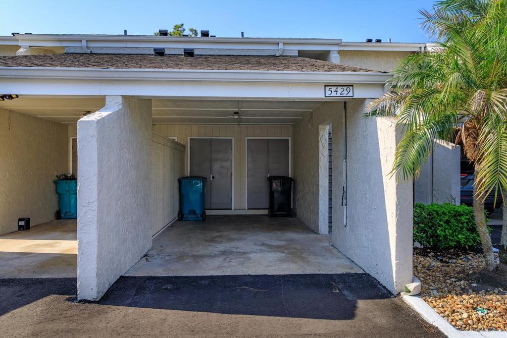 A covered carport features two storage closets and two trash bins under a shingled roof — 5429 VINELAND ROAD UNIT 6F, ORLANDO, FL