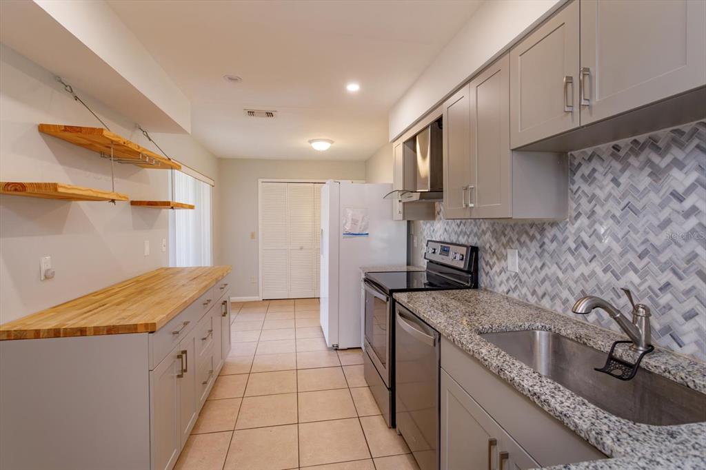 A kitchen features gray cabinets, granite countertops, a butcher block island, and a tiled backsplash — 5429 VINELAND ROAD UNIT 6F, ORLANDO, FL