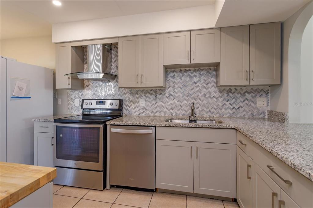 A kitchen features gray cabinets, granite countertops, stainless steel appliances, and a herringbone tile backsplash — 5429 VINELAND ROAD UNIT 6F, ORLANDO, FL
