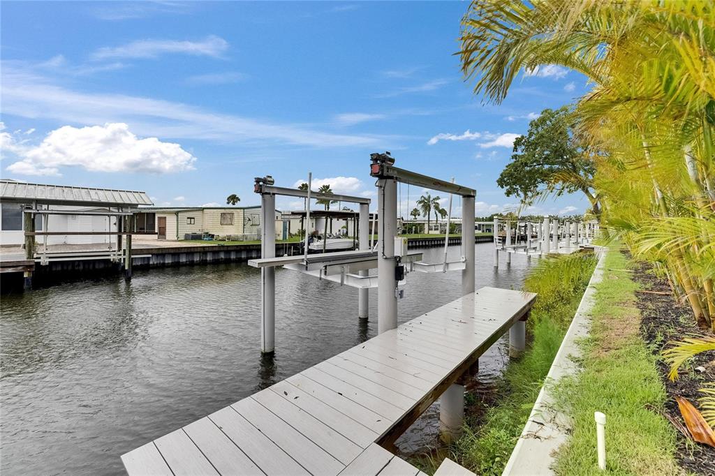 A boat lift and a wooden dock extend into a canal beside a grassy yard — 6528 SIMONE SHORES CIRCLE, APOLLO BEACH, FL