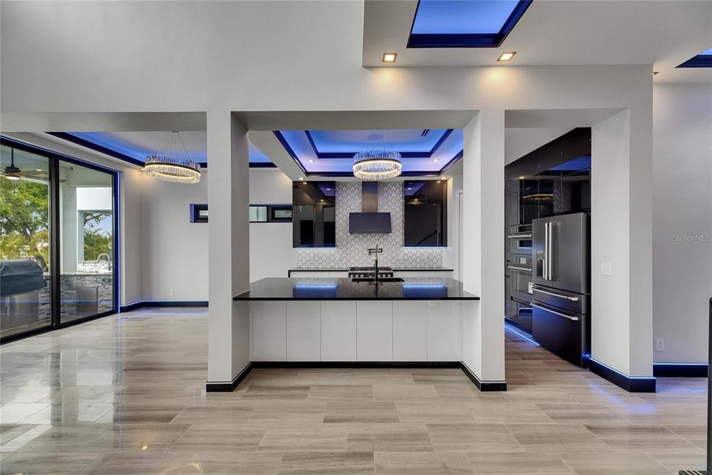 A modern kitchen features a black island, white cabinetry, blue cove lighting, and tile flooring — 6528 SIMONE SHORES CIRCLE, APOLLO BEACH, FL
