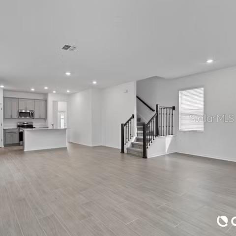 An open-concept living area features light wood-look tile flooring, a kitchen with gray cabinets, and stairs — 4123 CONJUNCTION WAY, APOPKA, FL