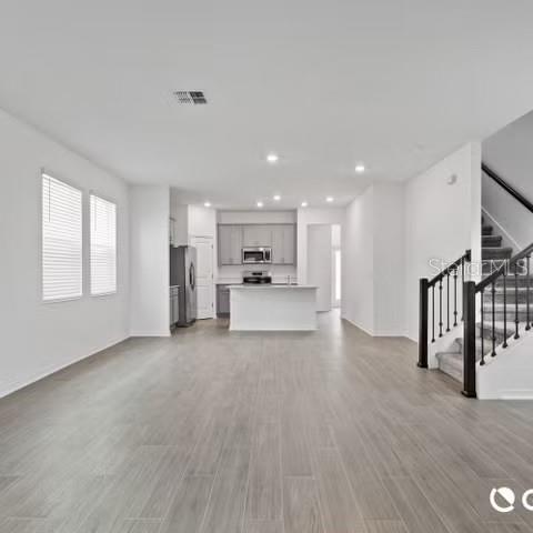 An open-concept living area features light wood-look flooring, white walls, and a staircase with railings — 4123 CONJUNCTION WAY, APOPKA, FL