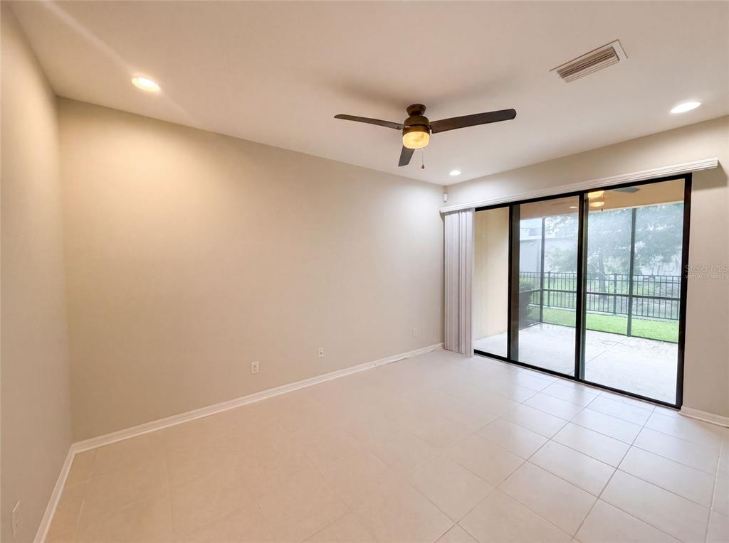 An empty room with tile flooring, a ceiling fan, and sliding glass doors to a patio — 4848 WANDERING WAY, WESLEY CHAPEL, FL