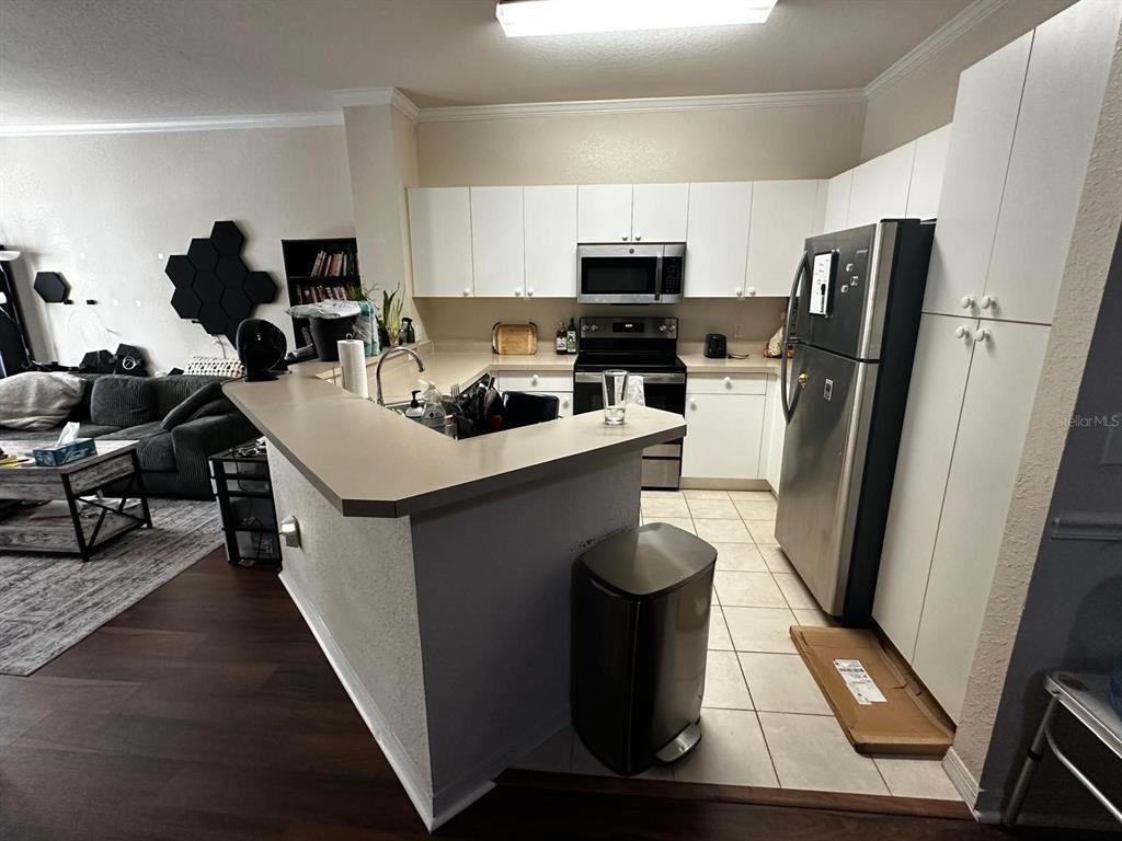 A kitchen with white cabinets, stainless steel appliances, and a breakfast bar overlooks a living area — 3605 CONROY ROAD UNIT 524, ORLANDO, FL
