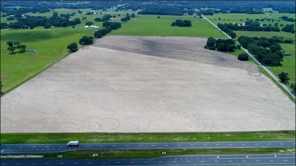An aerial view shows a large, cleared, sandy plot of land adjacent to a highway — US HIGHWAY 301, OXFORD, FL