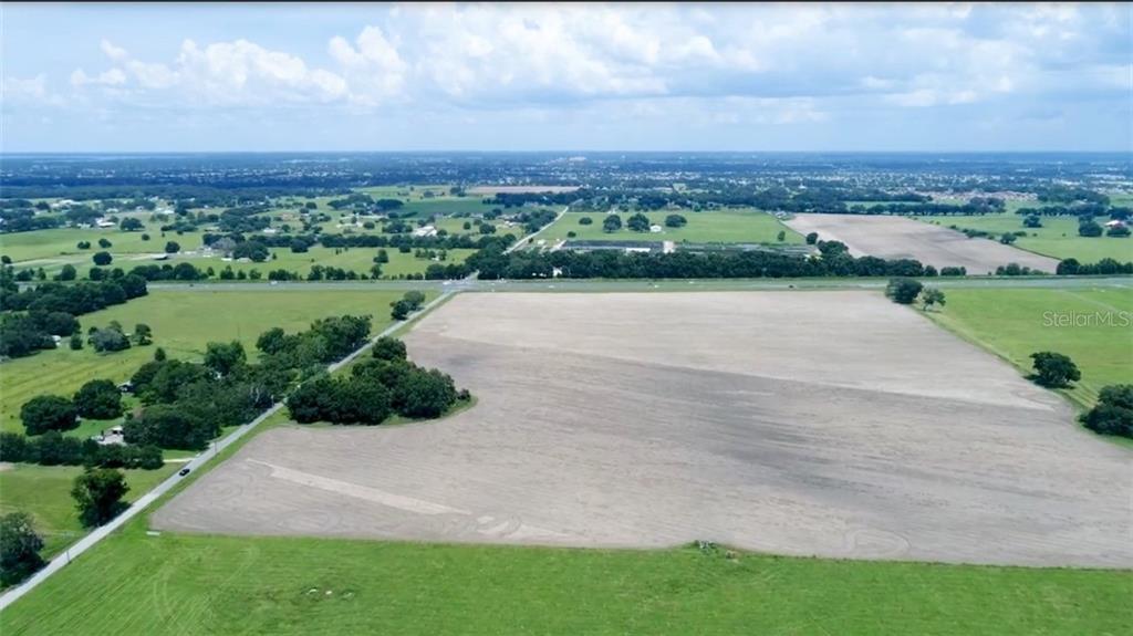 An aerial view shows a large, cleared agricultural field bordered by trees and a road — US HIGHWAY 301, OXFORD, FL