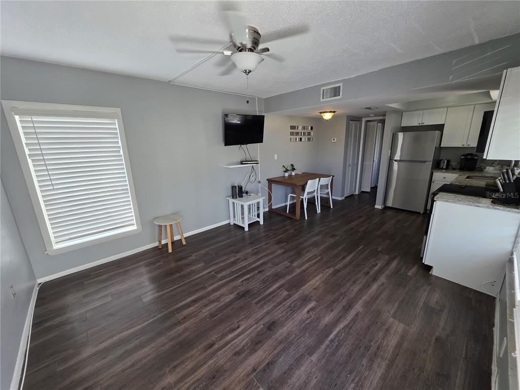 An open-concept living and dining area features dark wood-look flooring and a stainless steel refrigerator — 705 1ST STREET UNIT 4, INDIAN ROCKS BEACH, FL