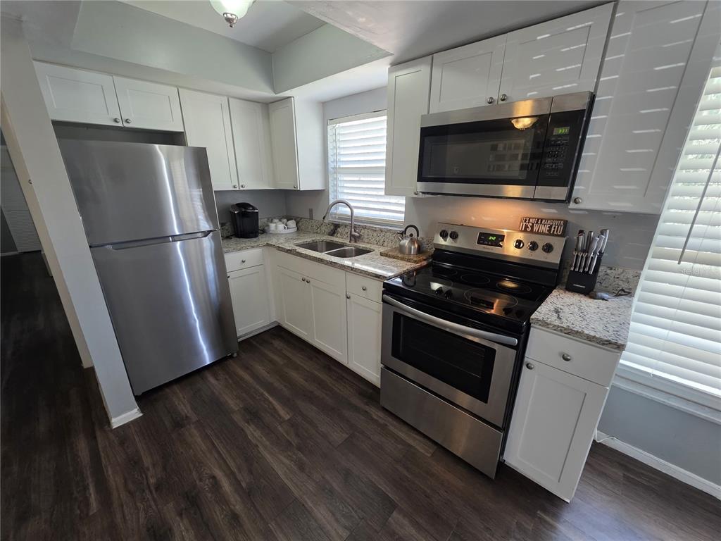 A kitchen features white cabinets, stainless steel appliances, and granite countertops over dark wood flooring — 705 1ST STREET UNIT 4, INDIAN ROCKS BEACH, FL