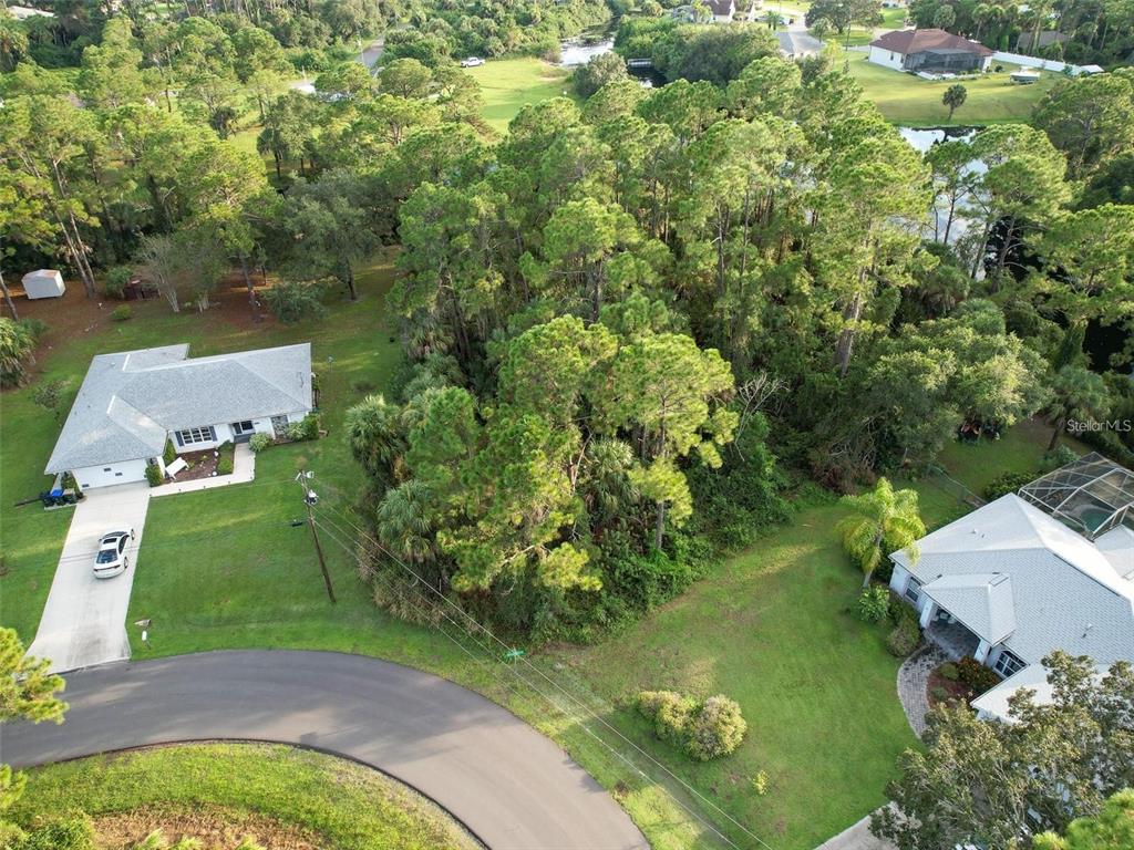 An aerial view shows two houses separated by a dense wooded lot and a curved road — Lot 19 ALBREN STREET, NORTH PORT, FL