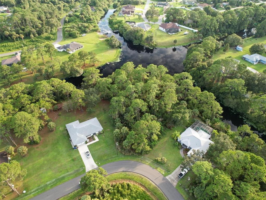 An aerial view shows two houses situated on a large, wooded lot near a canal — Lot 19 ALBREN STREET, NORTH PORT, FL