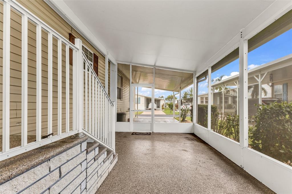 A covered, screened-in porch with concrete flooring, white railings, and stairs leading to the home — 1000 KINGS HIGHWAY UNIT 380, PORT CHARLOTTE, FL