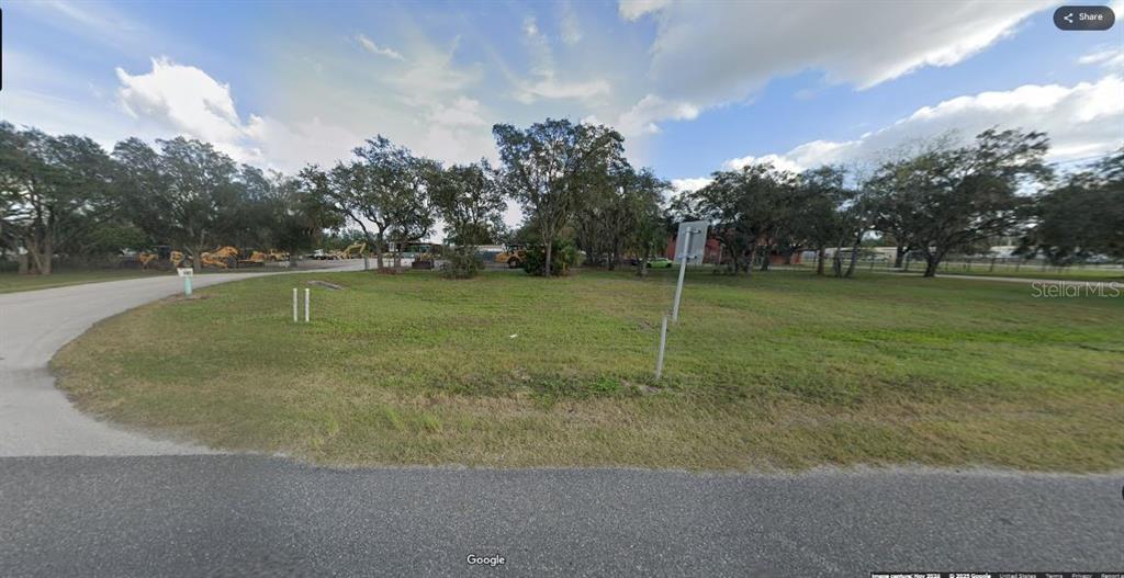 A vacant, grassy corner lot features several mature trees and a paved road — N/A, POLK CITY, FL