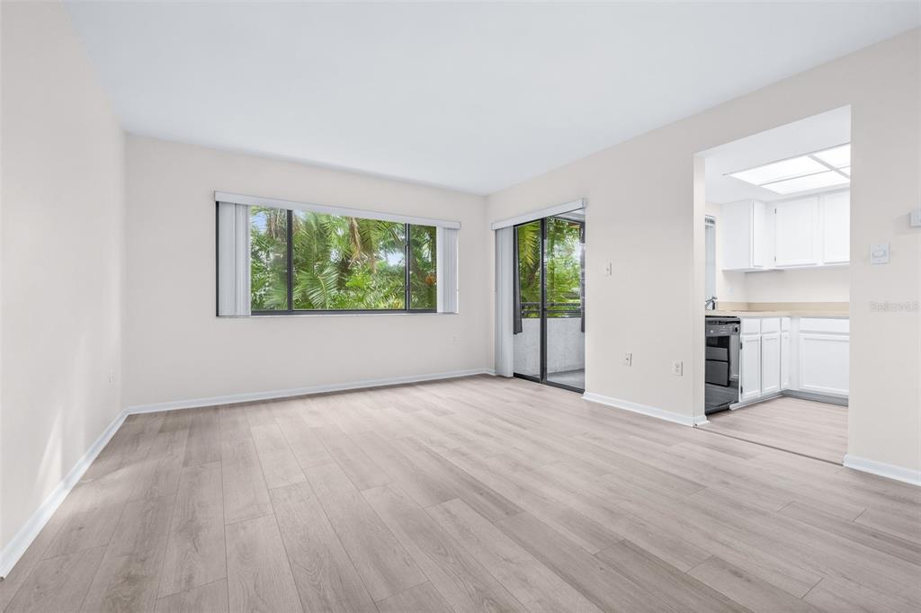 An empty living room with light wood-look flooring, a large window, and a sliding door — 13602 S VILLAGE DRIVE UNIT 1107, TAMPA, FL