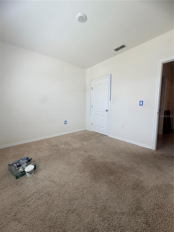 An empty bedroom features beige carpet, white walls, a white door, and painting supplies — 297 MEADOWBROOK BOULEVARD, WINTER HAVEN, FL