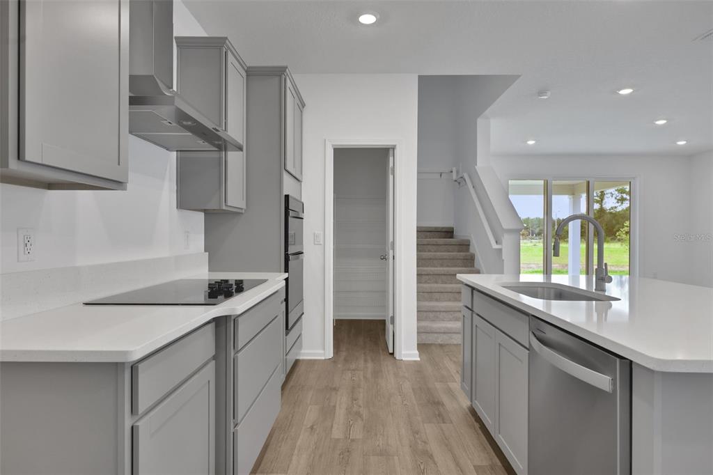 A modern kitchen features gray cabinets, white countertops, stainless steel appliances, and a staircase nearby — 3848 HOLSTEIN WAY, GREEN COVE SPRINGS, FL