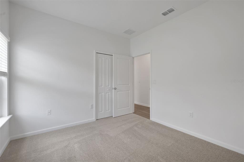 A bedroom features white walls, beige carpeting, a closet with double doors, and an open doorway — 3848 HOLSTEIN WAY, GREEN COVE SPRINGS, FL