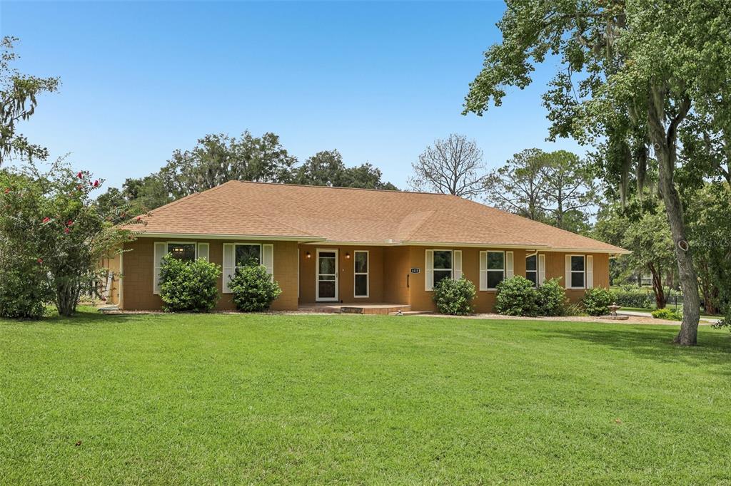 A single-story brick house with a brown shingled roof sits on a large grassy lawn — 4410 NW 76TH COURT, OCALA, FL