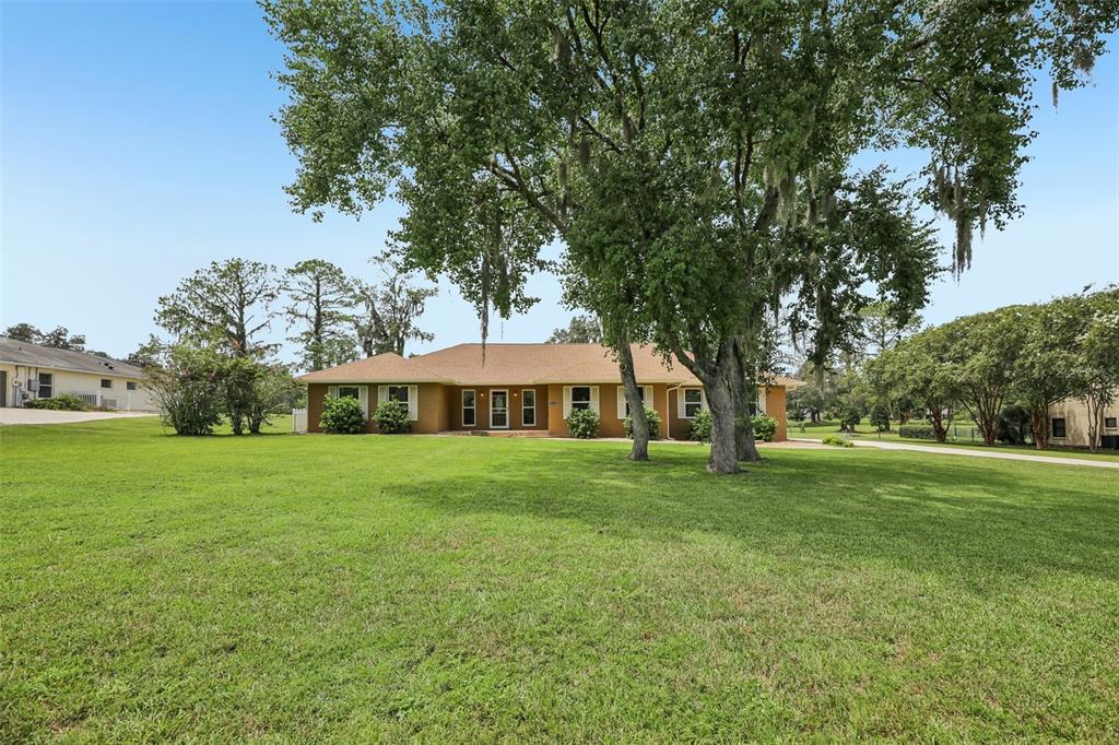 A single-story tan house with a brown roof sits on a large, grassy lawn — 4410 NW 76TH COURT, OCALA, FL