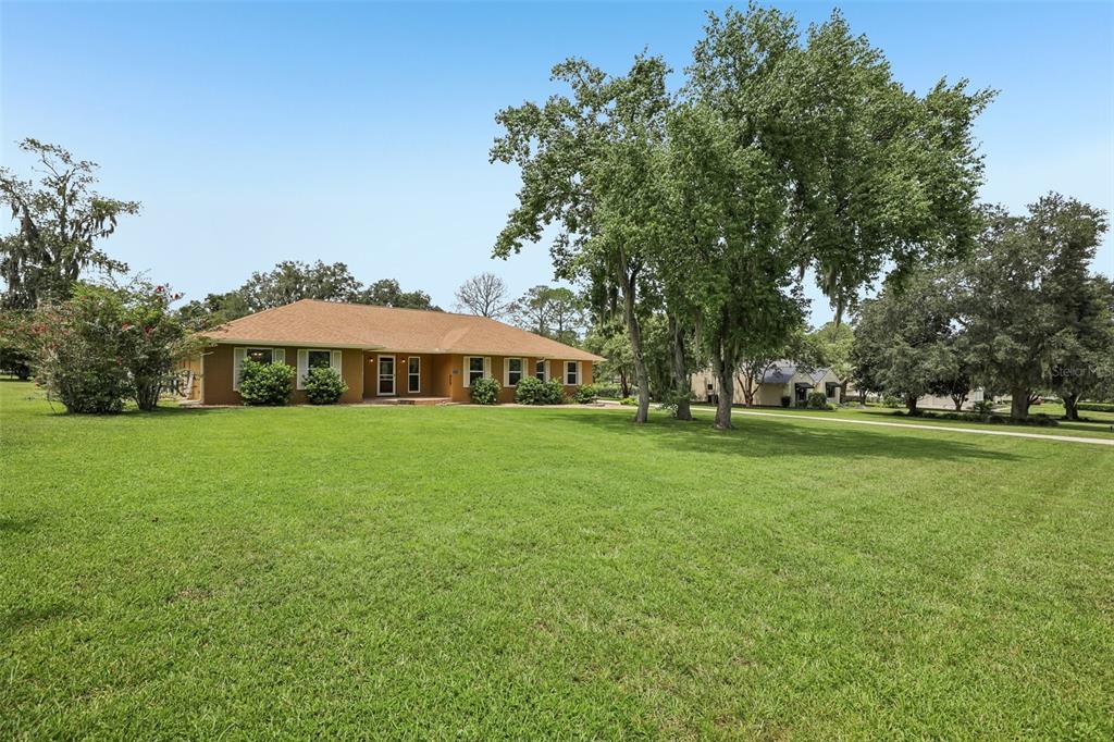 A single-story house with a brown roof sits on a large, grassy lawn with trees — 4410 NW 76TH COURT, OCALA, FL