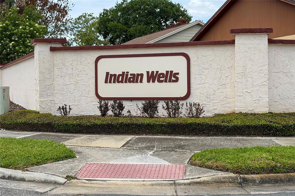 A white stucco wall features a sign reading Indian Wells above a manicured hedge — 3254 MOCCASIN DRIVE, KISSIMMEE, FL