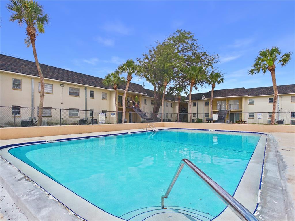A swimming pool sits in front of a two-story apartment building with palm trees — 2800 E 113TH AVENUE UNIT 213, TAMPA, FL