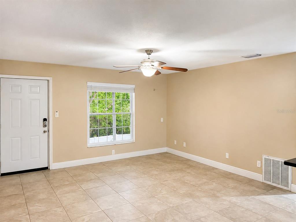 An empty room features beige walls, light-colored tile flooring, a ceiling fan, and a white door — 2800 E 113TH AVENUE UNIT 213, TAMPA, FL