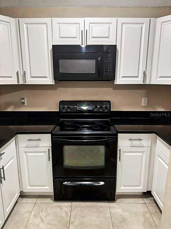 A kitchen features white cabinets, a black microwave, and a black electric range — 2800 E 113TH AVENUE UNIT 213, TAMPA, FL