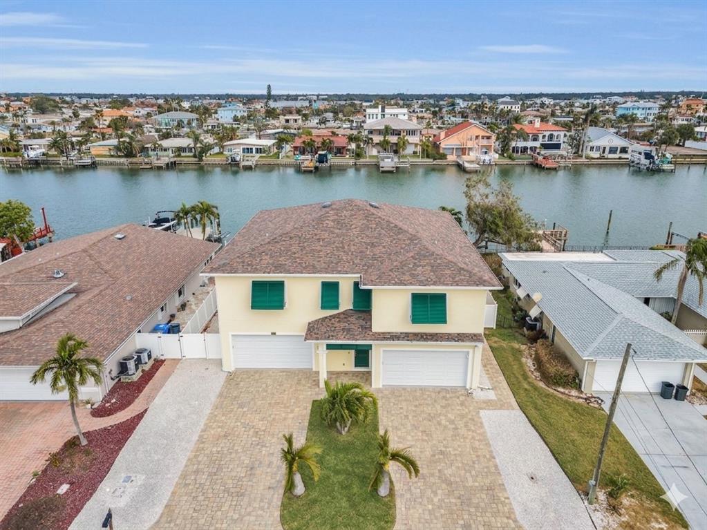 An aerial view of a two-story waterfront house with a paved driveway and green shutters — 11325 5TH STREET E, TREASURE ISLAND, FL