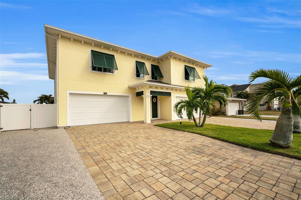 A two-story yellow house with a paver driveway, white garage door, and green window shutters — 11325 5TH STREET E, TREASURE ISLAND, FL