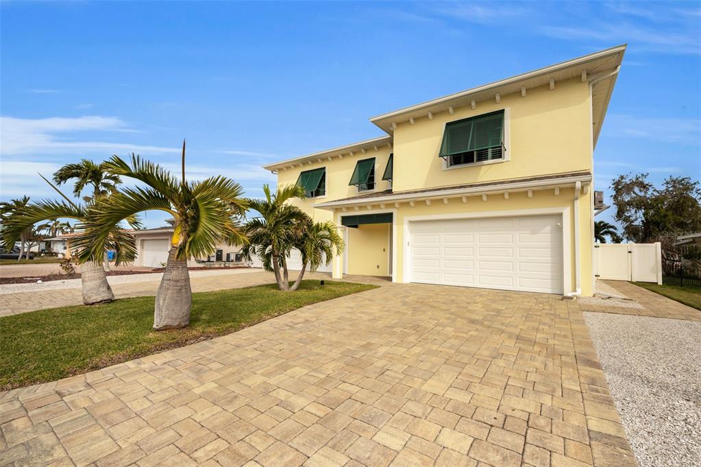 A two-story yellow house with a paver driveway, green shutters, and palm trees in front — 11325 5TH STREET E, TREASURE ISLAND, FL
