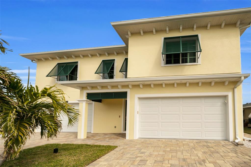 A two-story yellow house with a paved driveway, a two-car garage, and green window shutters — 11325 5TH STREET E, TREASURE ISLAND, FL