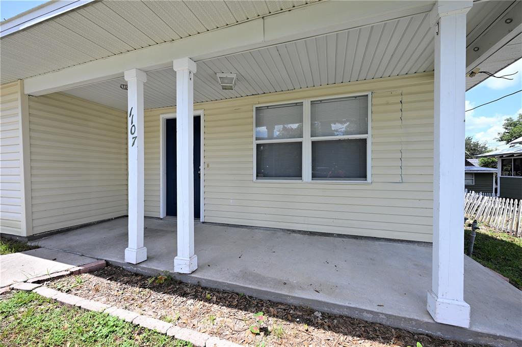 A covered concrete porch features white support columns and light yellow horizontal siding — 1107 KING AVENUE, LAKELAND, FL