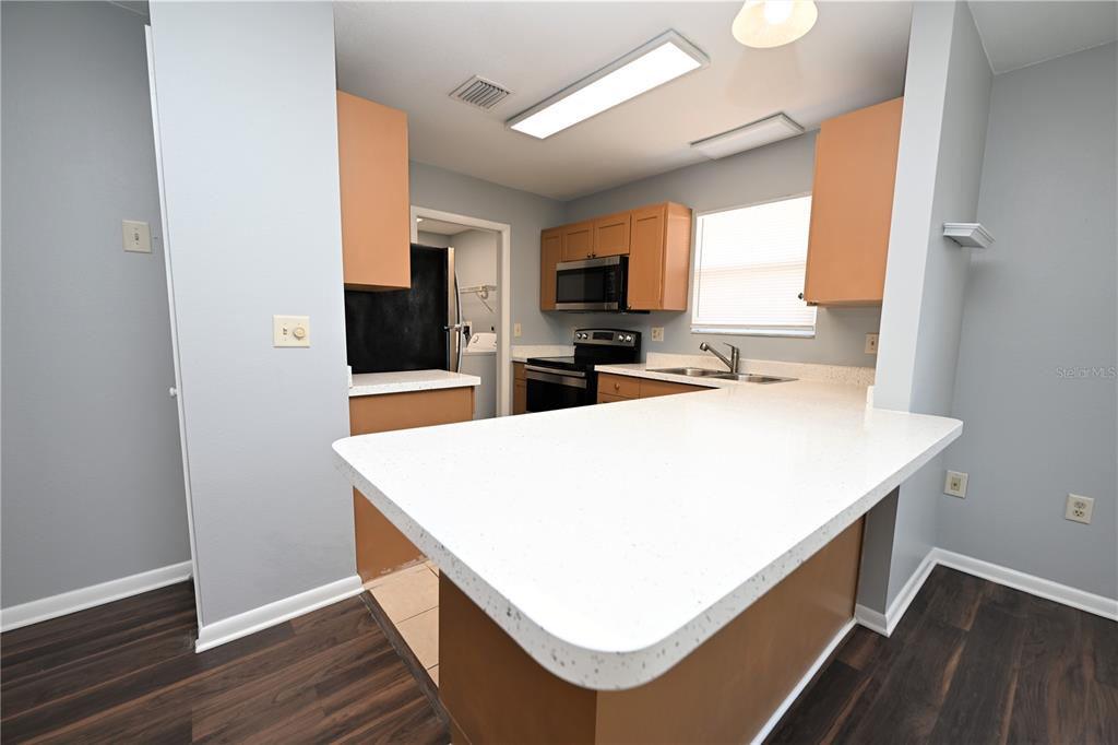 A kitchen features light-colored countertops, wood cabinets, stainless steel appliances, and dark wood flooring — 1107 KING AVENUE, LAKELAND, FL