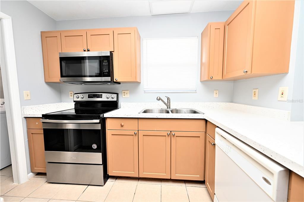 A kitchen features light wood cabinets, stainless steel appliances, white countertops, and tiled flooring — 1107 KING AVENUE, LAKELAND, FL
