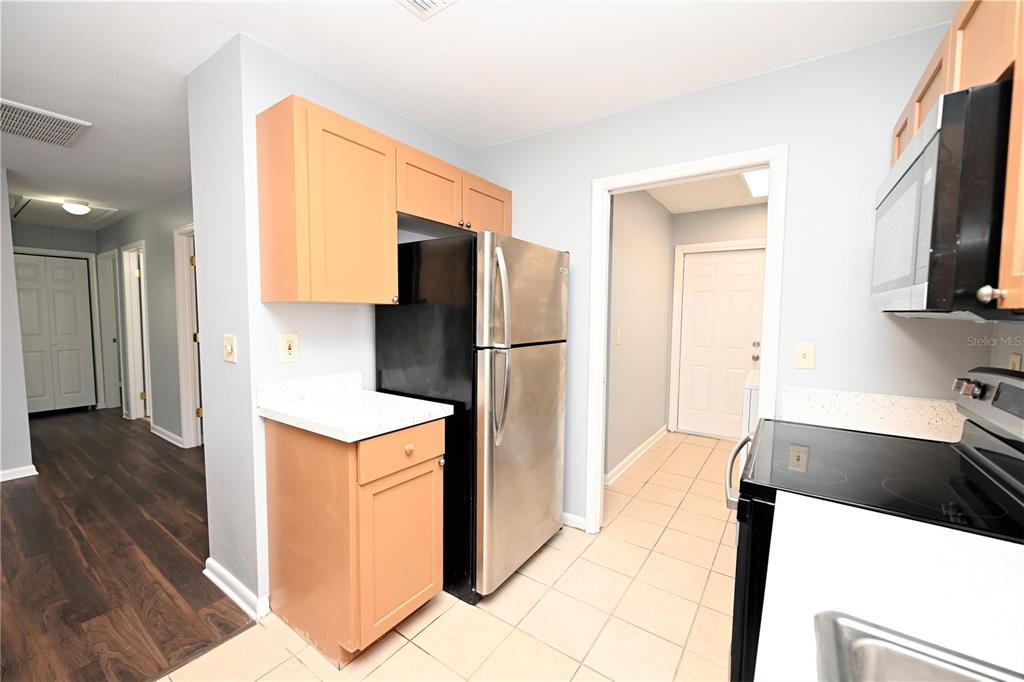 A kitchen features light wood cabinets, stainless steel appliances, and tile flooring — 1107 KING AVENUE, LAKELAND, FL