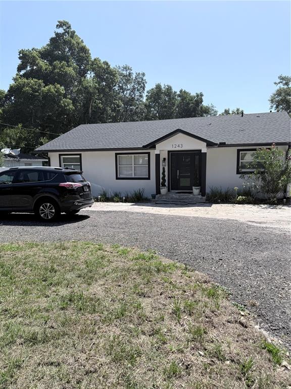 A single-story house with white stucco walls, a dark roof, and a gravel driveway — 1243 DINGENS AVENUE, WINDERMERE, FL
