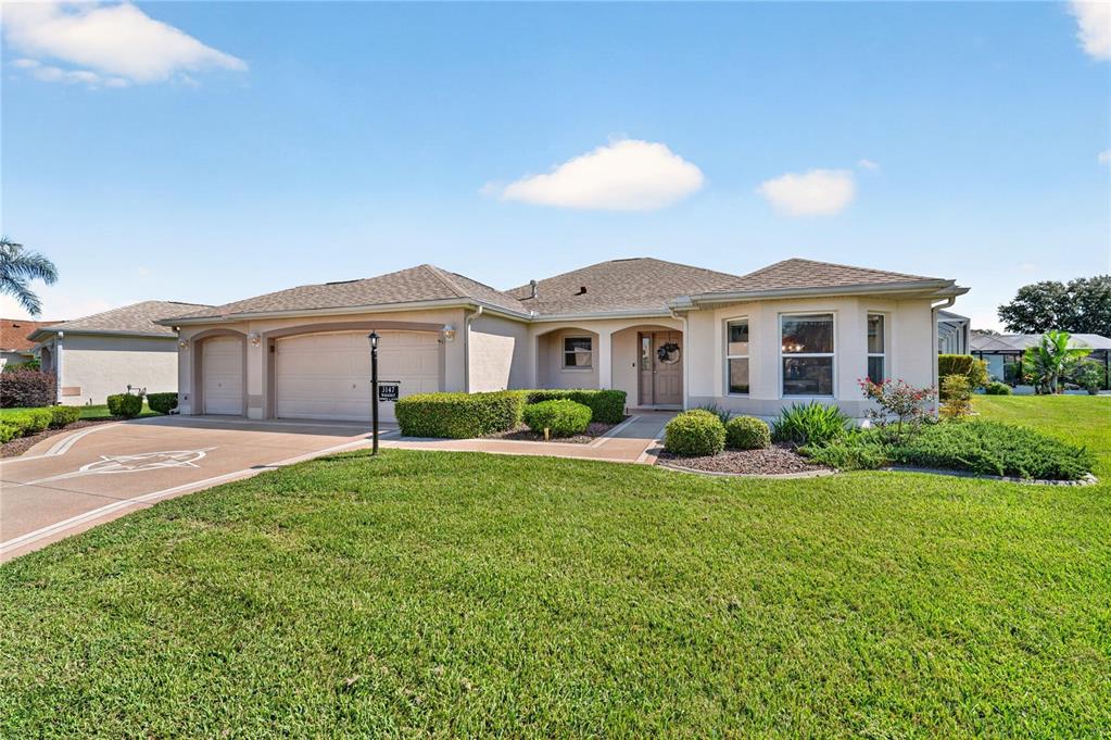 A single-story suburban house with a tan stucco exterior, a three-car garage, and landscaped lawn — 3147 MANSFIELD STREET, THE VILLAGES, FL