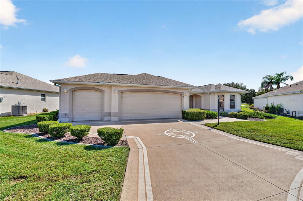 A single-story house with a three-car garage and a compass rose painted on the driveway — 3147 MANSFIELD STREET, THE VILLAGES, FL
