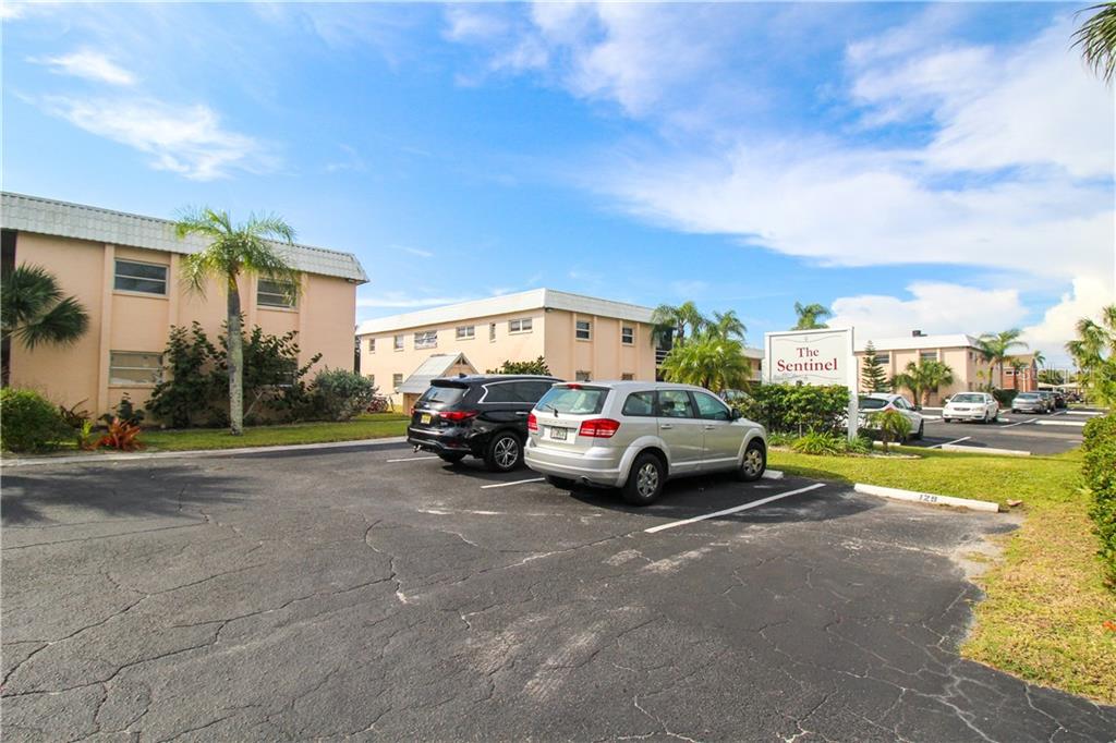 A parking lot sits in front of The Sentinel apartment buildings under a blue sky — 460 BASE AVENUE E UNIT 125, VENICE, FL