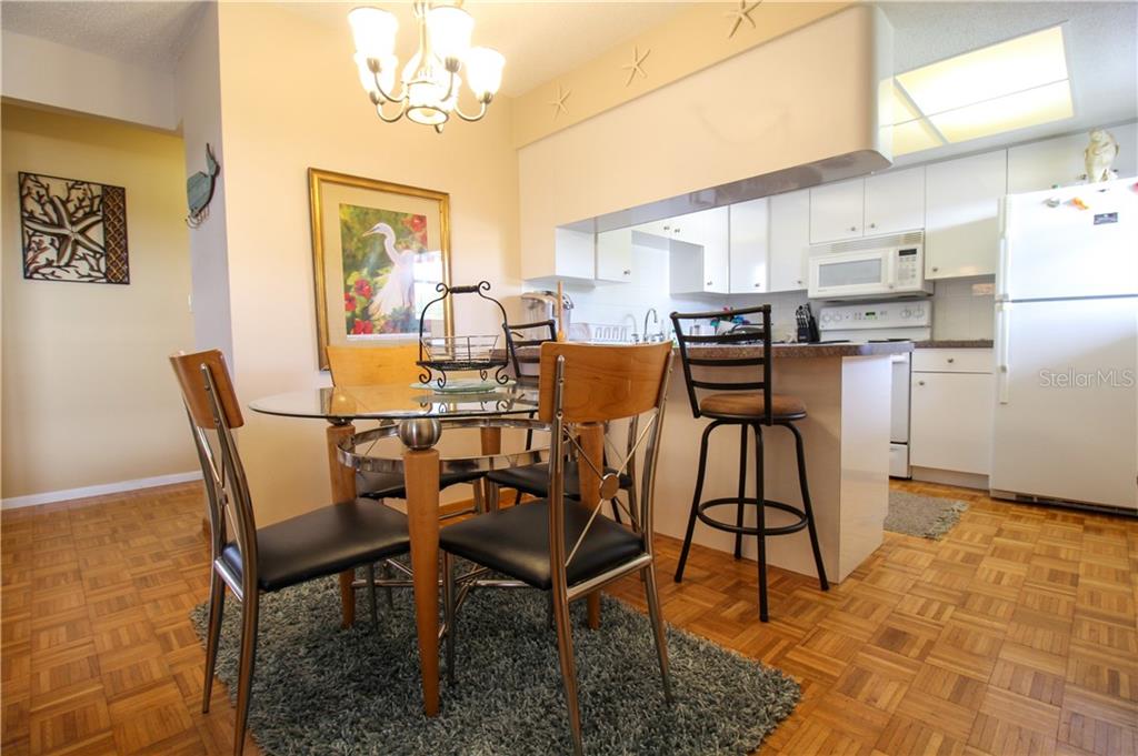 A dining area with a glass table and chairs sits adjacent to a white kitchen — 460 BASE AVENUE E UNIT 125, VENICE, FL