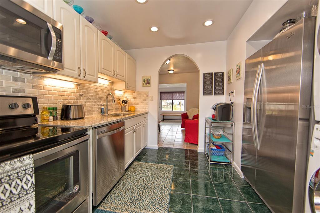 A kitchen with white cabinets, stainless steel appliances, granite countertops, and dark green tile floors — 839 3RD STREET N, SAFETY HARBOR, FL