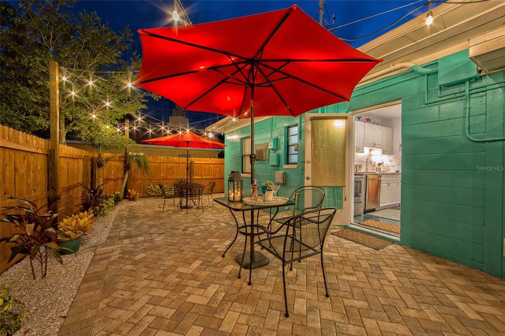 A paved patio features two red umbrellas, outdoor furniture, and string lights at night — 839 3RD STREET N, SAFETY HARBOR, FL