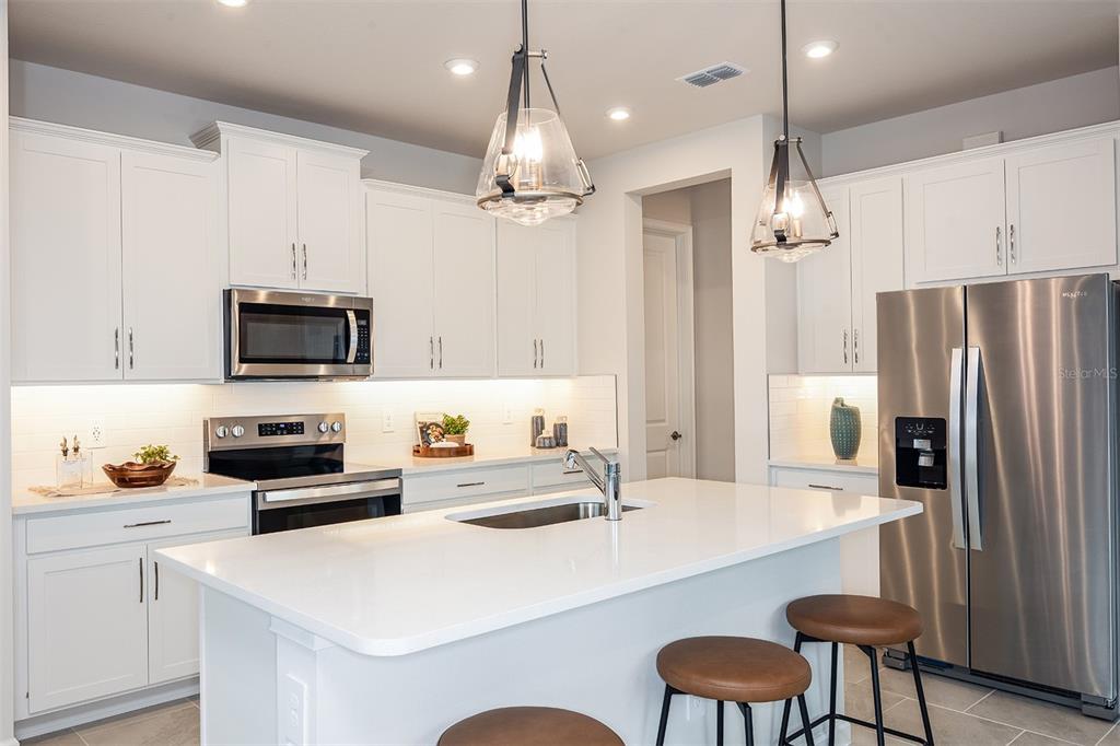 A modern kitchen features white cabinetry, stainless steel appliances, a center island, and pendant lighting — 1706 SOARING VIDA STREET, PALMETTO, FL