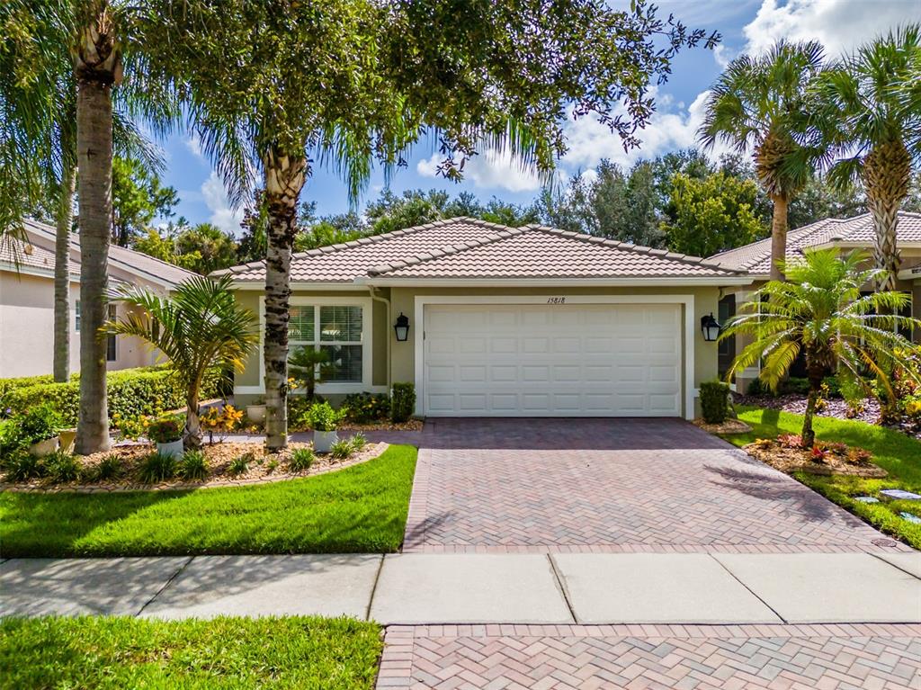 A single-story house with a white garage door, tiled roof, and palm trees in the yard — 15818 COBBLE MILL DRIVE, WIMAUMA, FL