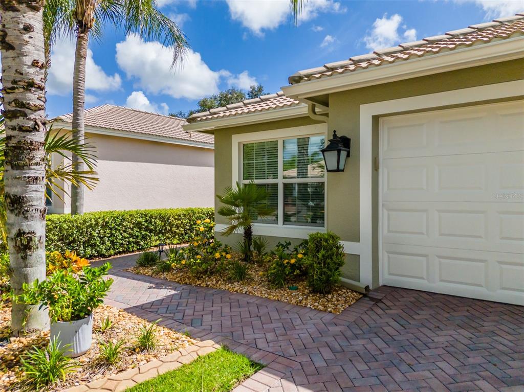 A paved walkway leads to the side of a house with a garage and landscaping — 15818 COBBLE MILL DRIVE, WIMAUMA, FL