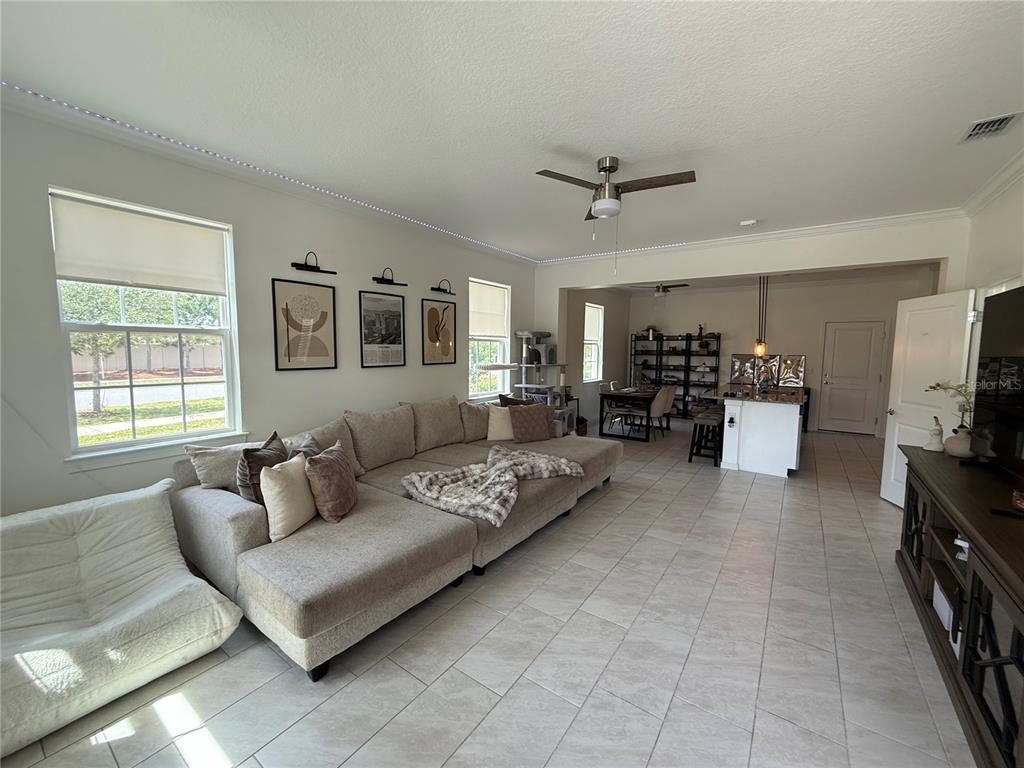 A living room with a large sectional sofa, tile flooring, and an open kitchen area — 14486 SAPELO BEACH DRIVE, ORLANDO, FL
