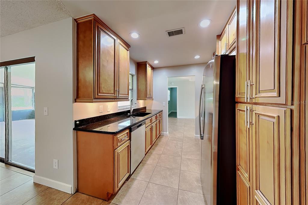 A kitchen features wood cabinets, black countertops, stainless steel appliances, and light-colored tile flooring — 1016 MANCHESTER CIRCLE, WINTER PARK, FL